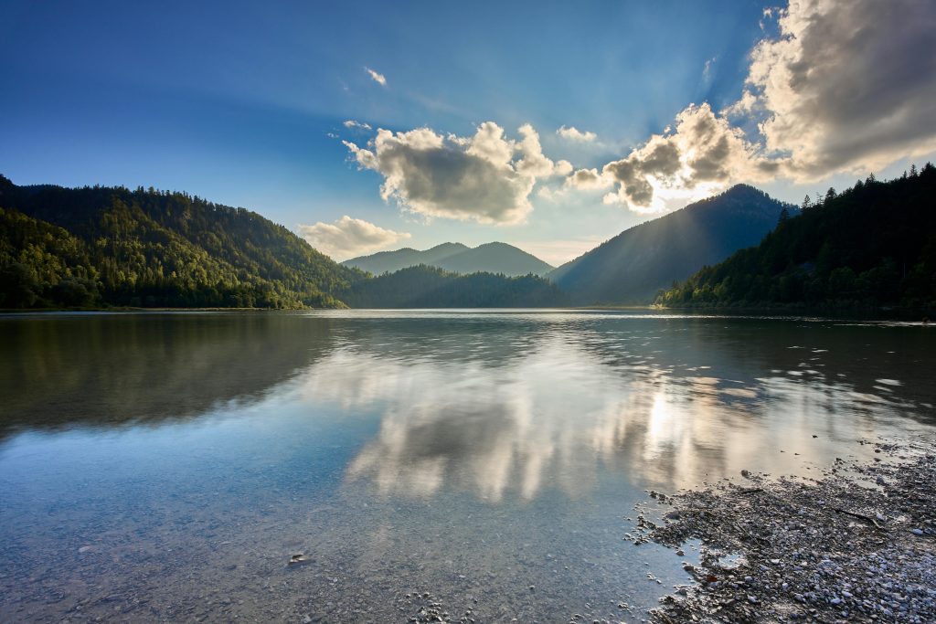 Scenic view of a serene lake reflecting mountains and clouds in Reit im Winkl, Bavaria.